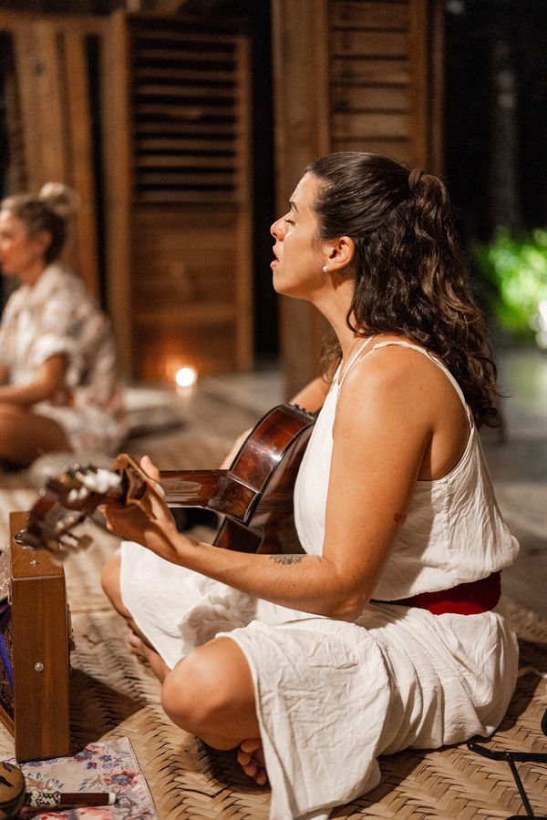 A woman singing and playing guitar during an evening circle