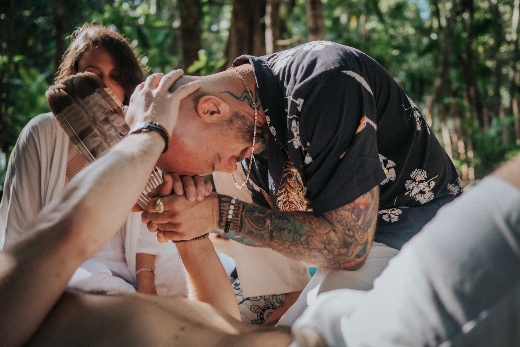 A facilitator bowing his head over clasped hands with a participant in a Bufo ceremony