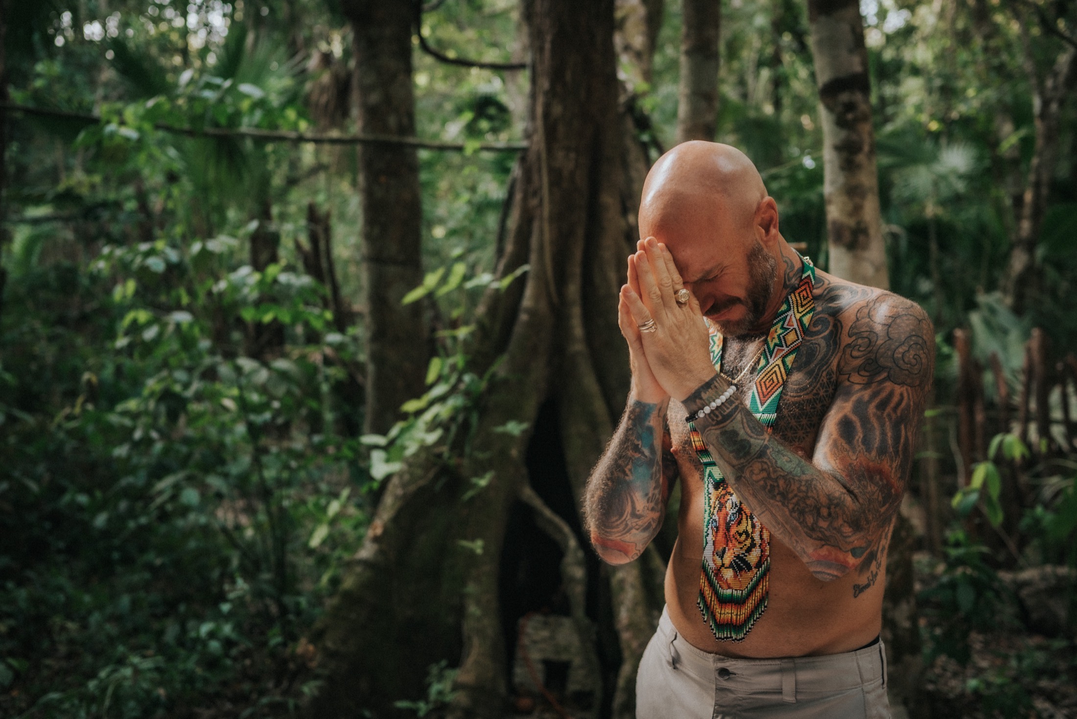 A facilitator in prayer in the jungle before a Bufo ceremony, wearing beaded Tiger regalia