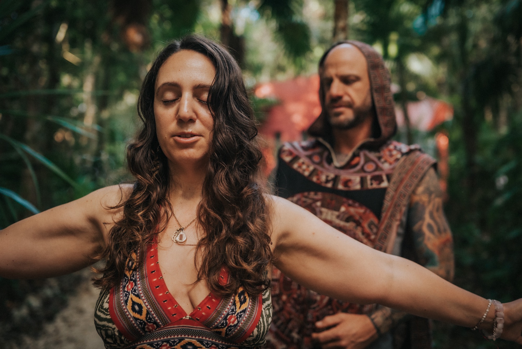 A woman opening her arms with eyes closed, held by a facilitator in the jungle