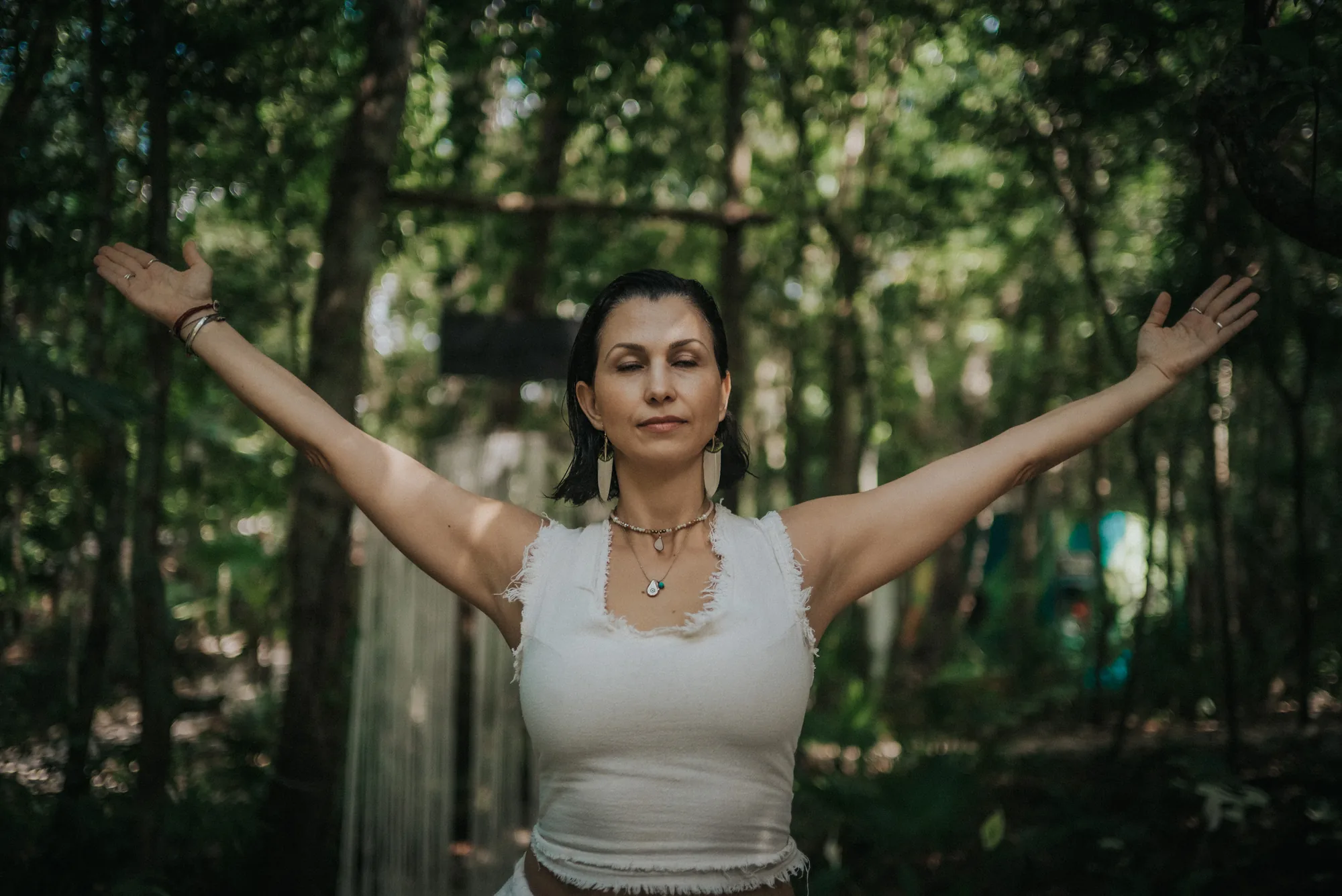 A woman standing in the jungle with her arms open and eyes closed